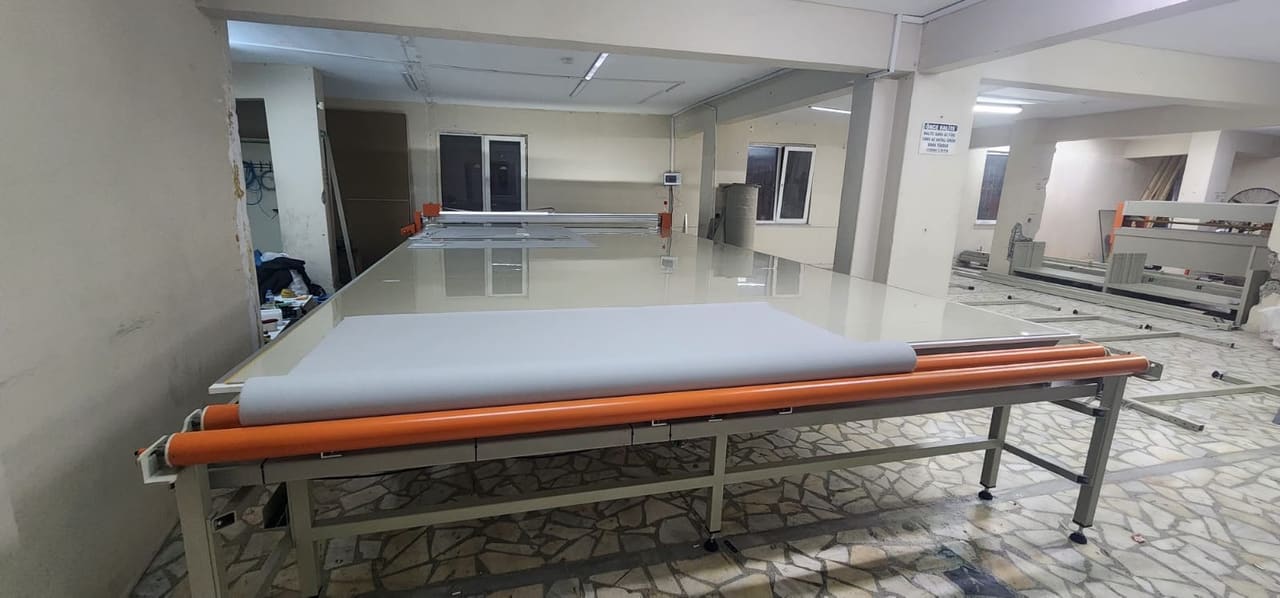 میز برش پارچه صنعتی CNC با رول پارچه بارگذاری‌شده روی میز گسترش